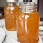 Two mason jars are full of the Instant Pot beef broth in front of the Instant Pot.