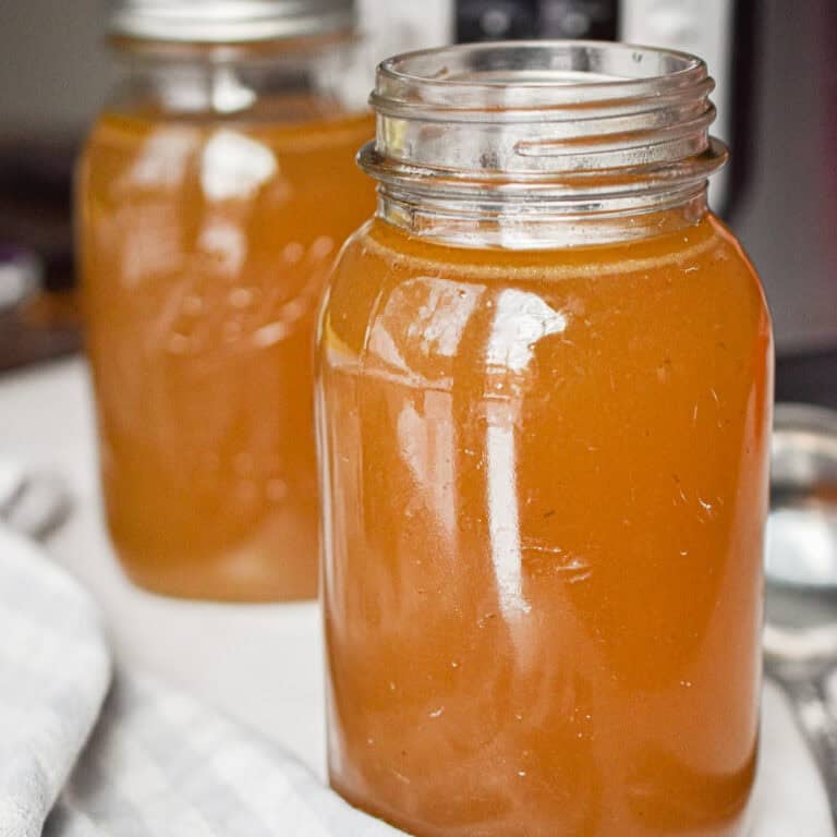 Two mason jars are full of the Instant Pot beef broth in front of the Instant Pot.