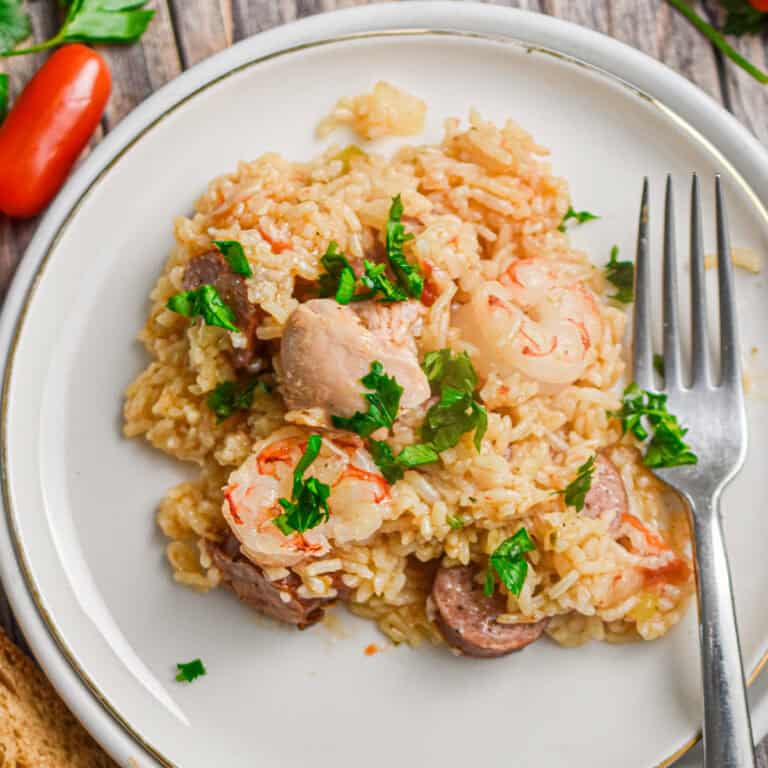 The Instant Pot Jambalaya is on a plate with a fork surrounded by parsley and tomatoes.