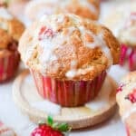 Icing is on top of the sourdough strawberry muffin surrounded by muffins and strawberries.