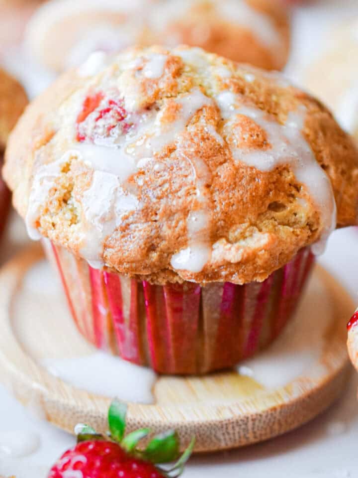 Icing is on top of the sourdough strawberry muffin surrounded by muffins and strawberries.