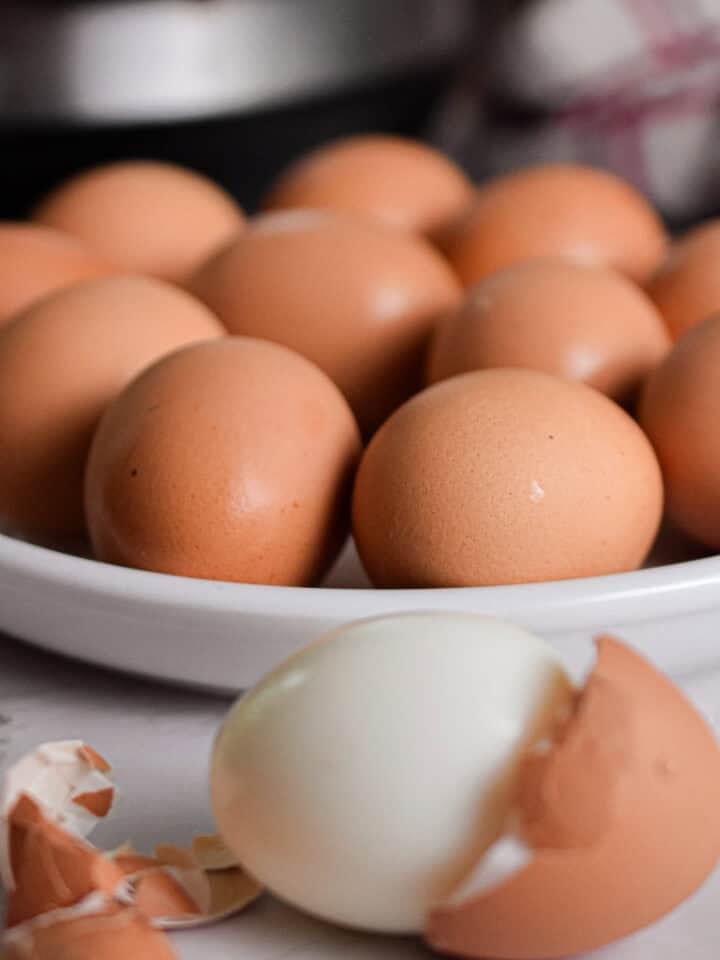 One egg is peeled in front of a plate of hard boiled eggs and the Instant Pot.