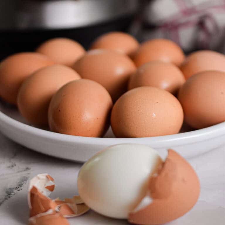 One egg is peeled in front of a plate of hard boiled eggs and the Instant Pot.