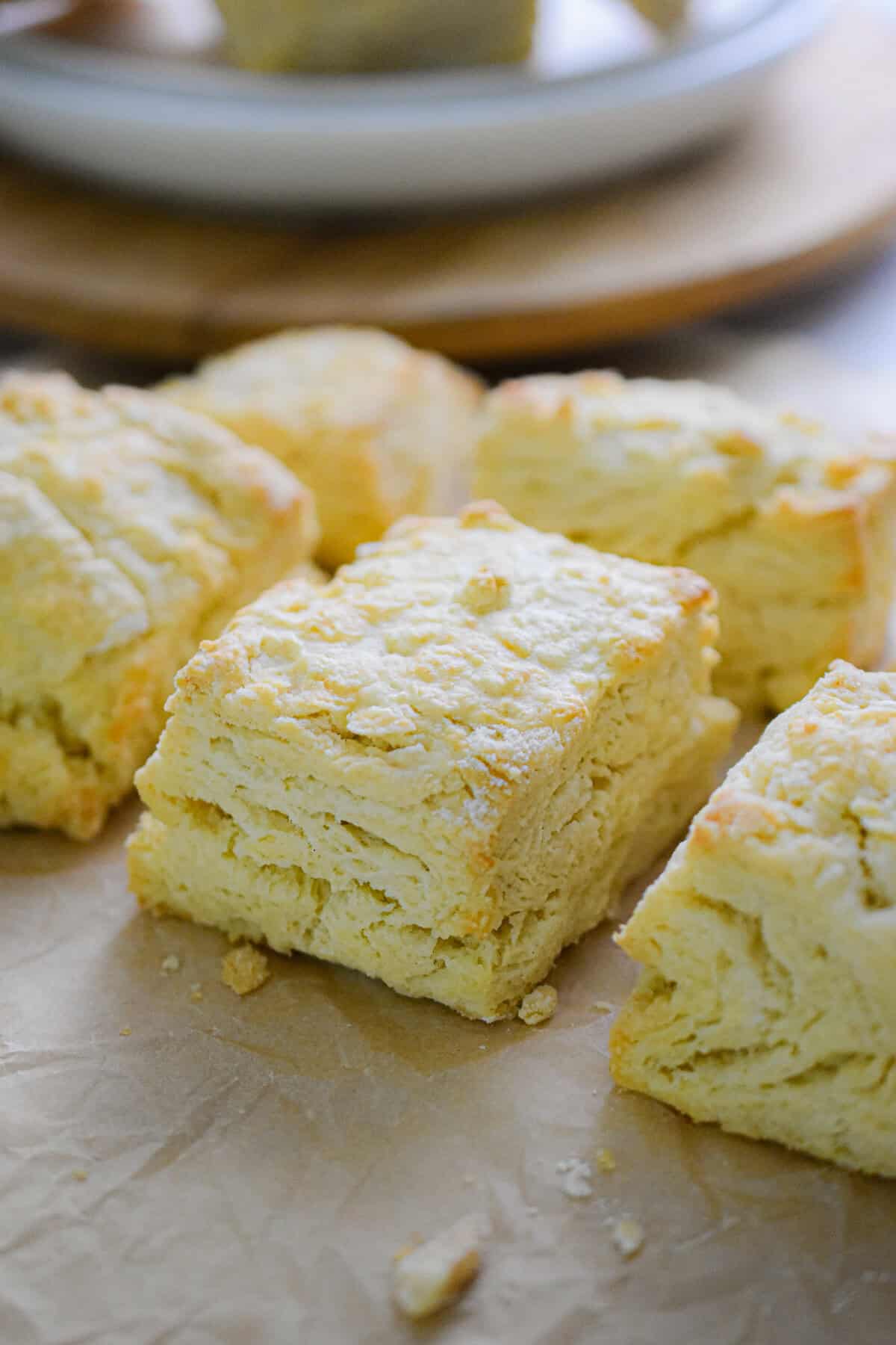 Six biscuits with self rising flour are on a piece of parchment paper with a plate in the background.