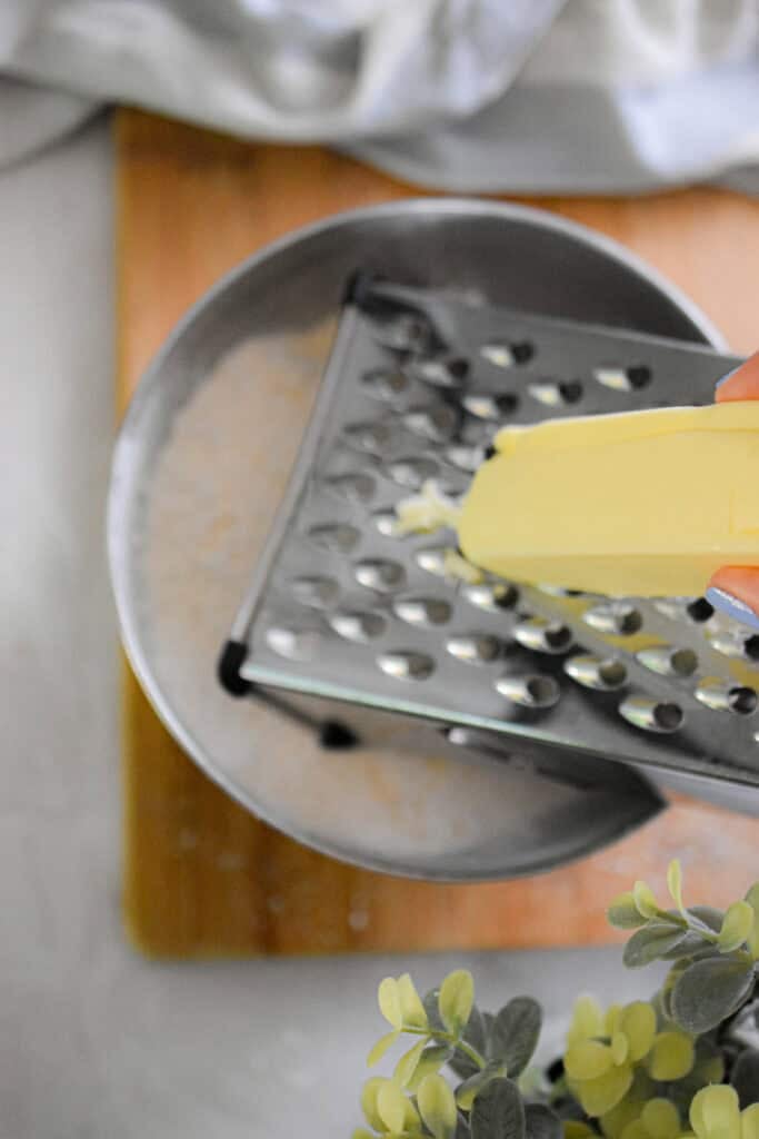 The butter is being grated over a bowl of flour.