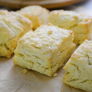 Six biscuits with self rising flour are on a piece of parchment paper all next to each other.