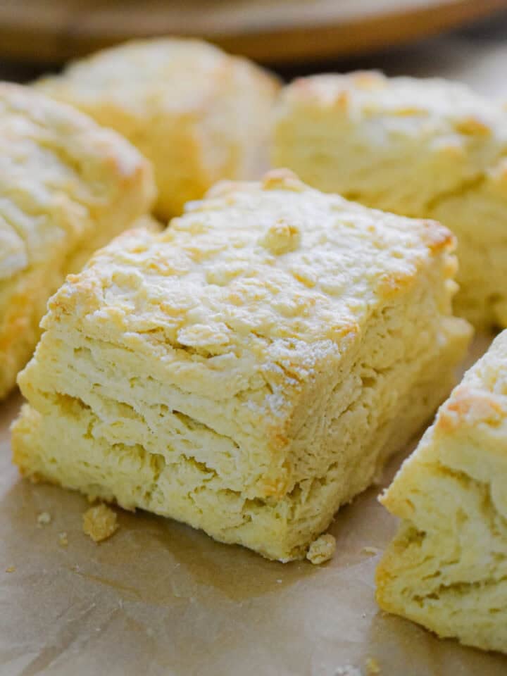 Six biscuits with self rising flour are on a piece of parchment paper all next to each other.