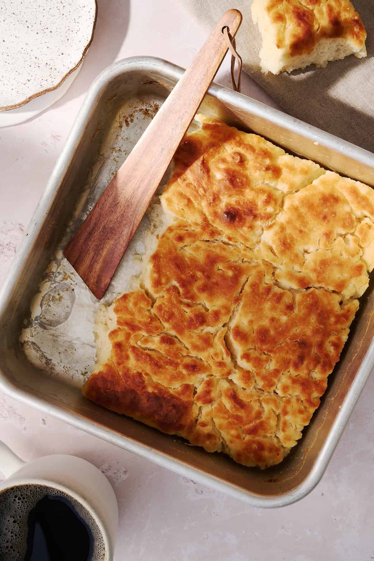 The butter swim biscuits are in a square pan with a wooden spoon in the pan.