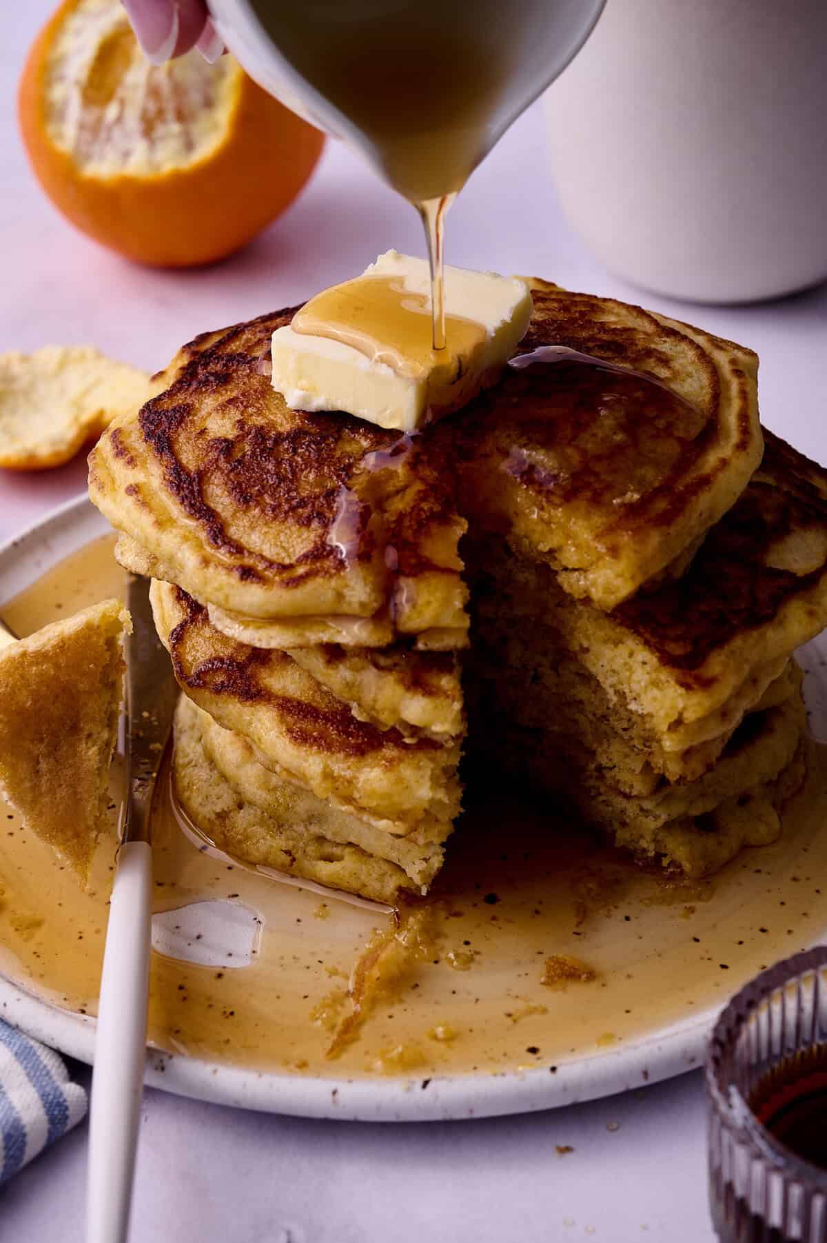 Maple syrup is being poured into a stack of the cornmeal pancakes with a slice of the stack cut out.