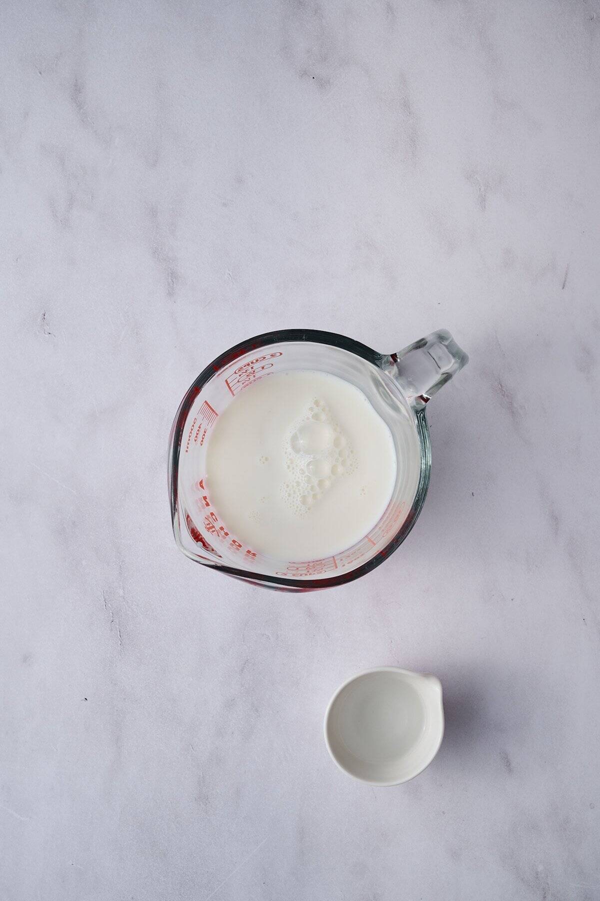 The milk is in a liquid measuring cup next to a small container of vinegar.