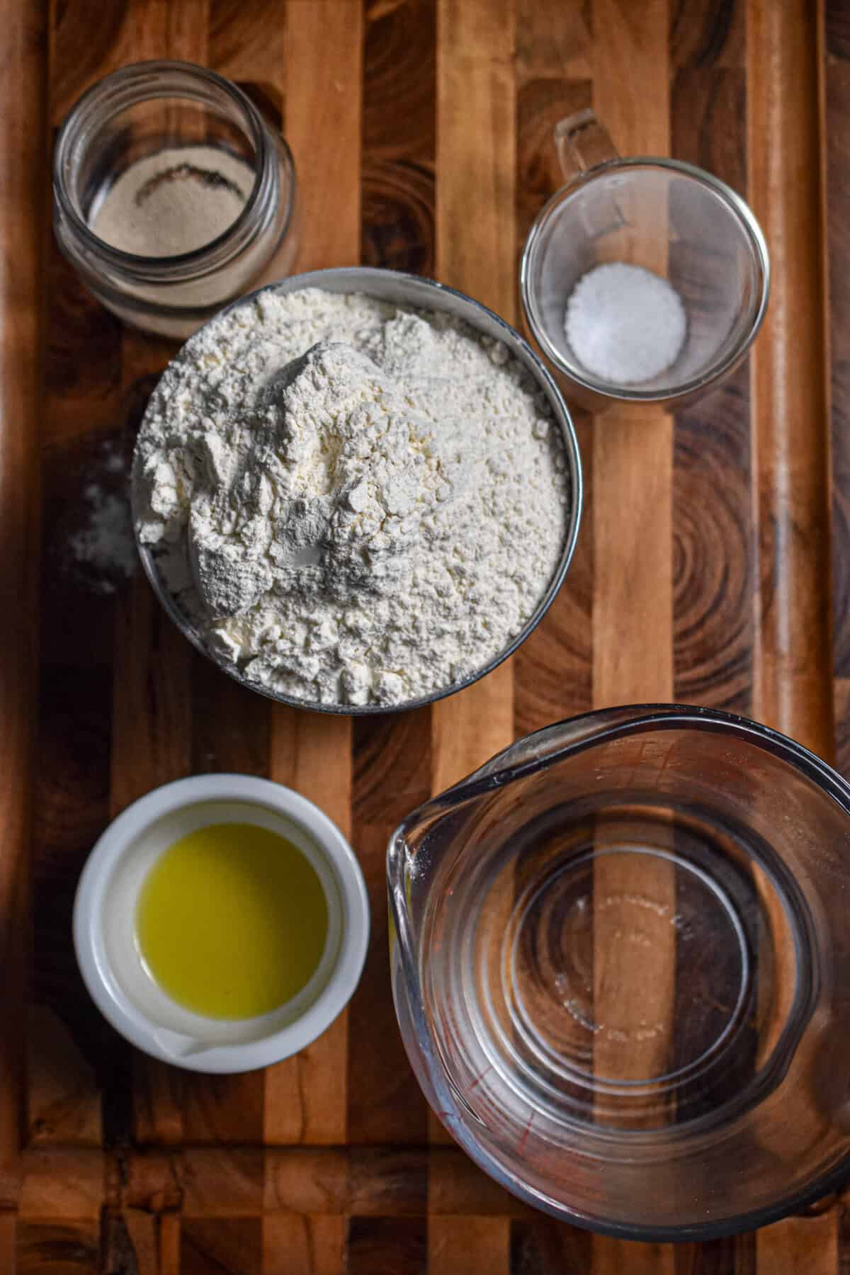 The ingredients for the ciabatta loaf are laid out on a wooden cutting board.
