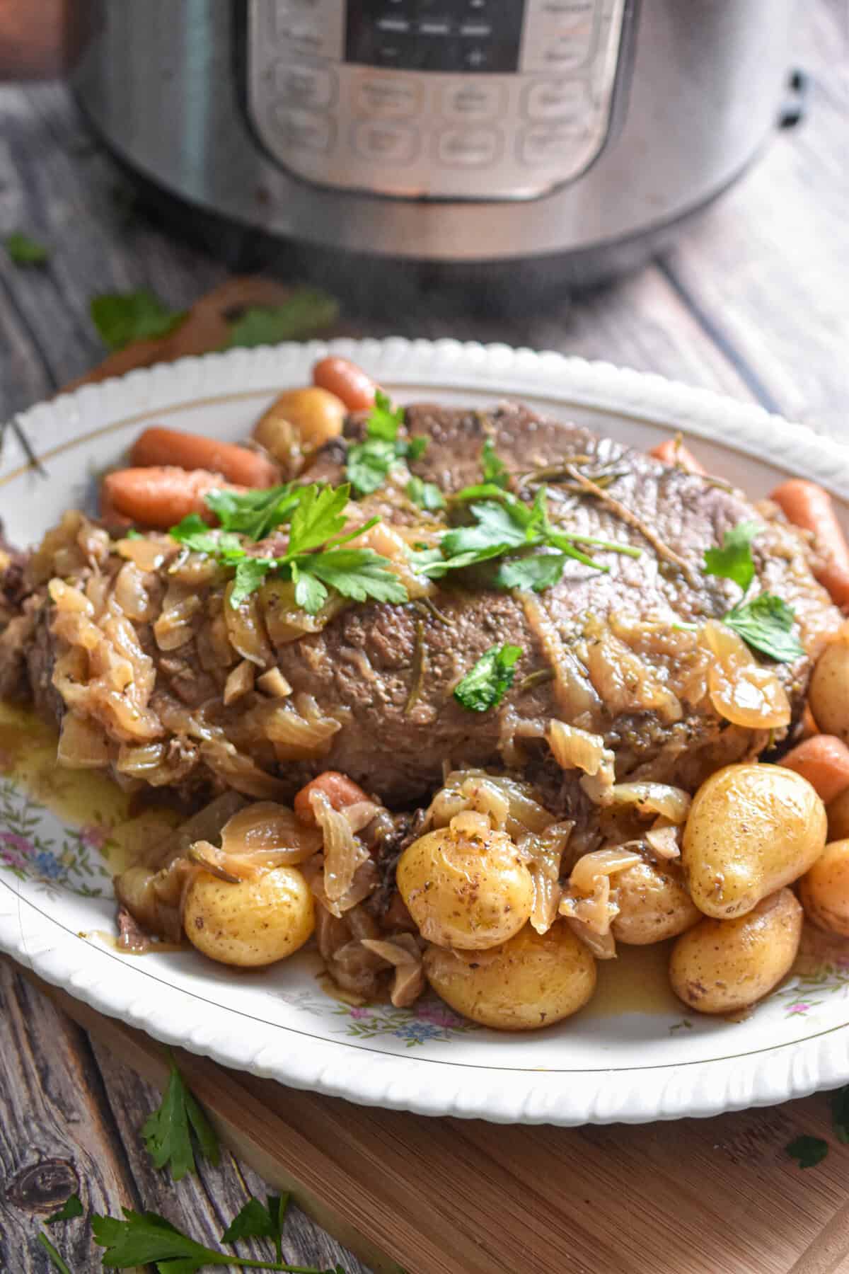 The vegetables and potatoes surround the meat on a plate on a cutting board.