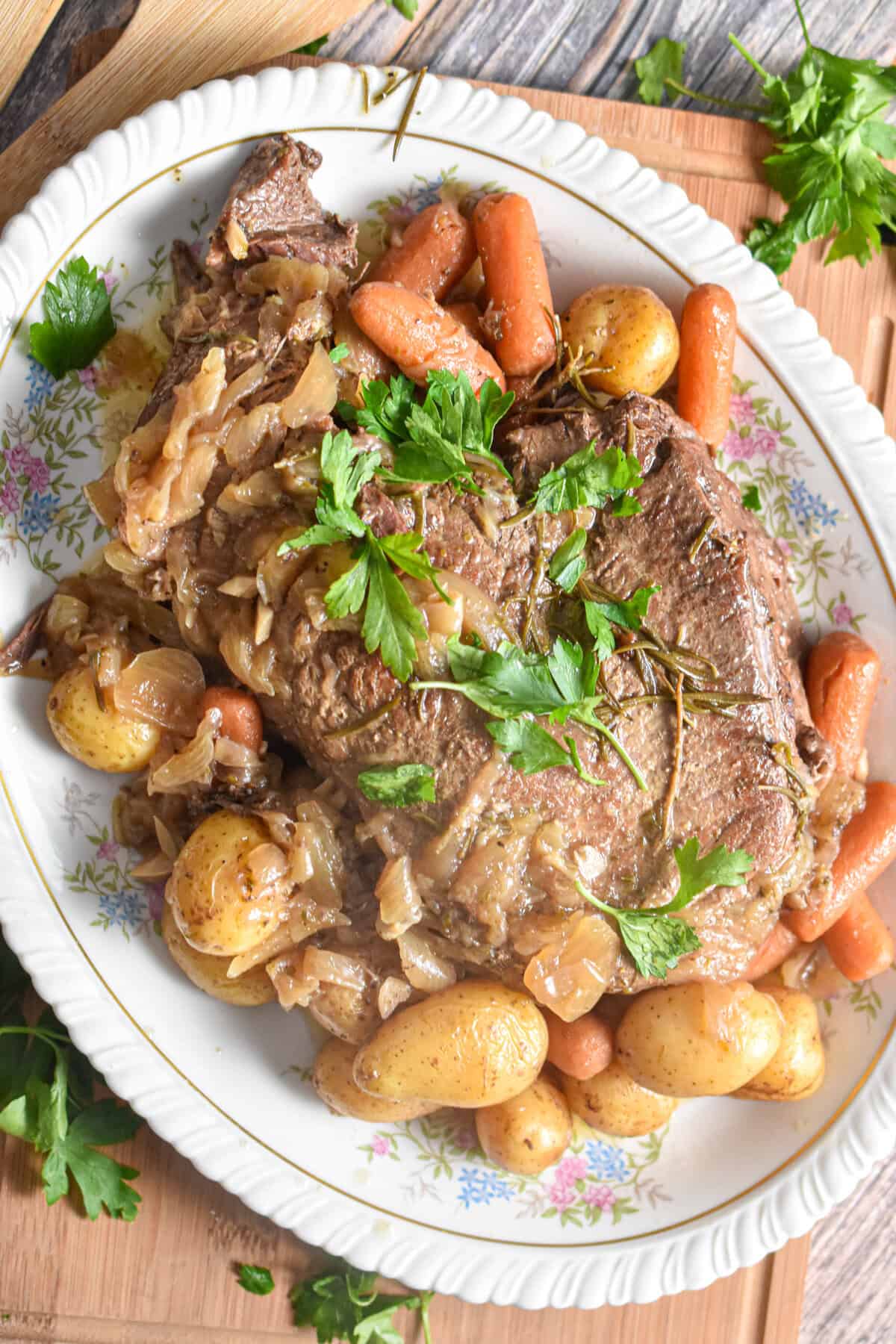 Baby carrots and baby potatoes are surrounding the roast on a floral plate.