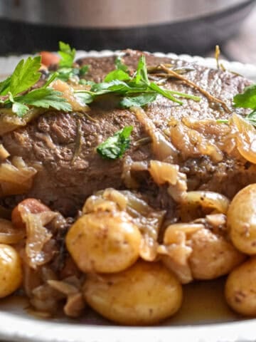 The baby potatoes are surrounding the pot roast in front of an Instant Pot.