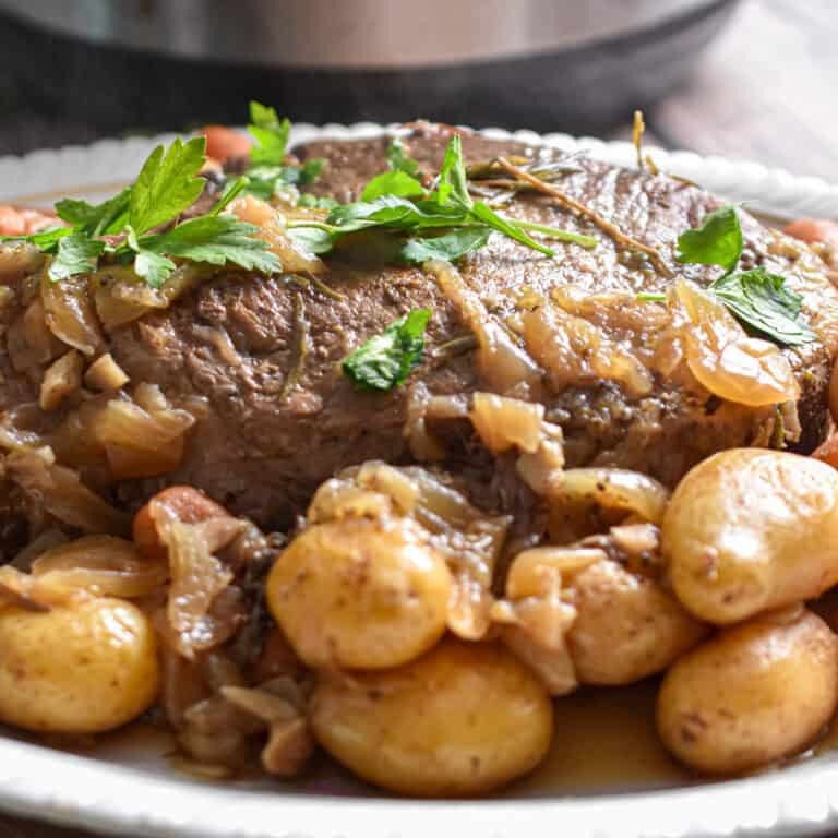 The baby potatoes are surrounding the pot roast in front of an Instant Pot.