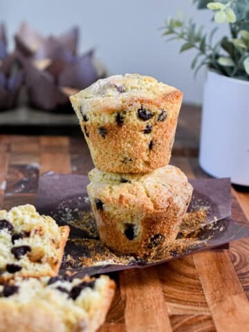 A chocolate chip muffin with self rising flour is cut in half on in front of a tower of two muffins on top of each other.