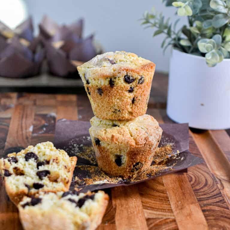 A chocolate chip muffin with self rising flour is cut in half on in front of a tower of two muffins on top of each other.