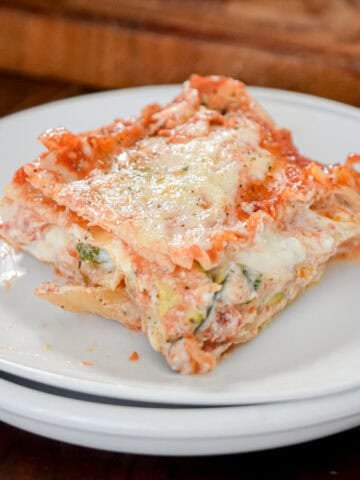 A slice of the vegetable lasagna is on white plates with a cutting board behind it.