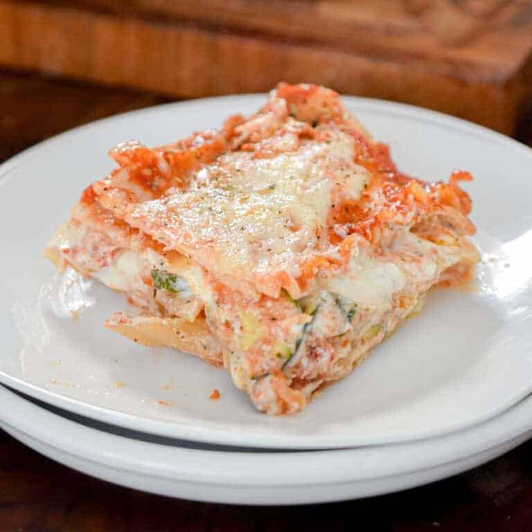 A slice of the vegetable lasagna is on white plates with a cutting board behind it.