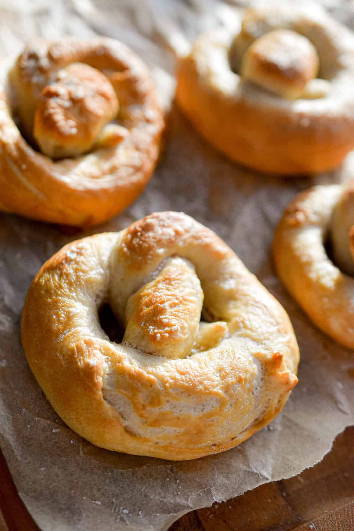 Four sourdough pretzels are on a parchment lined cutting board.