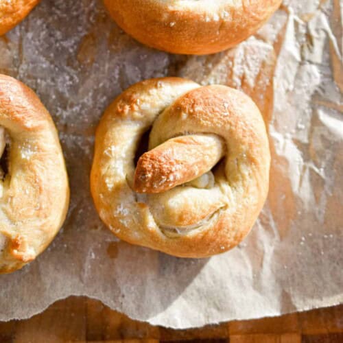 A sourdough pretzel is next to some other pretzels on a piece of parchment paper on top of a cutting board.