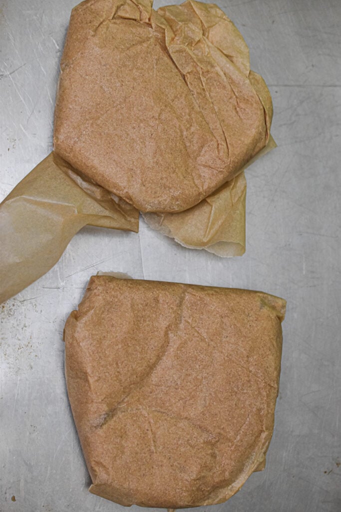 Two discs of the dough are wrapped in parchment paper and on a baking sheet.