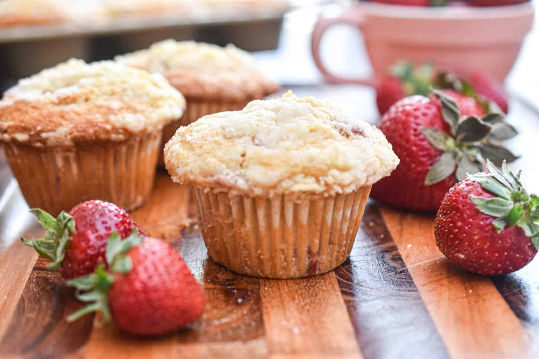 The muffin is surrounded by other muffins and strawberries on a wooden cutting board.