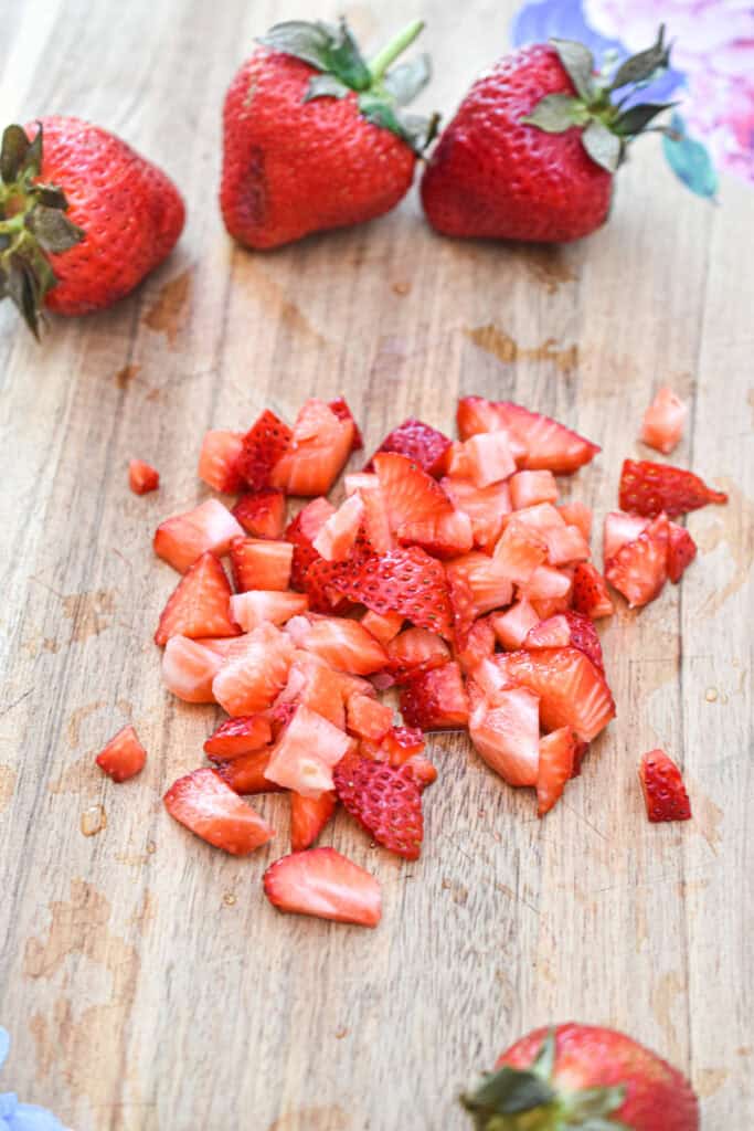 Fresh strawberries and chopped strawberries on a wooden surface.