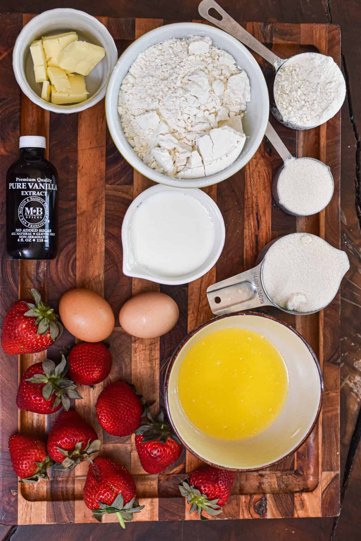 Fresh ingredients for bakery-style strawberry muffins with butter, eggs, flour, and strawberries.