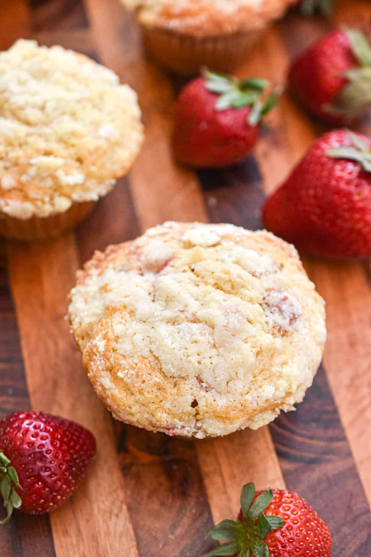 Strawberries surround two muffins on a wooden cutting board.