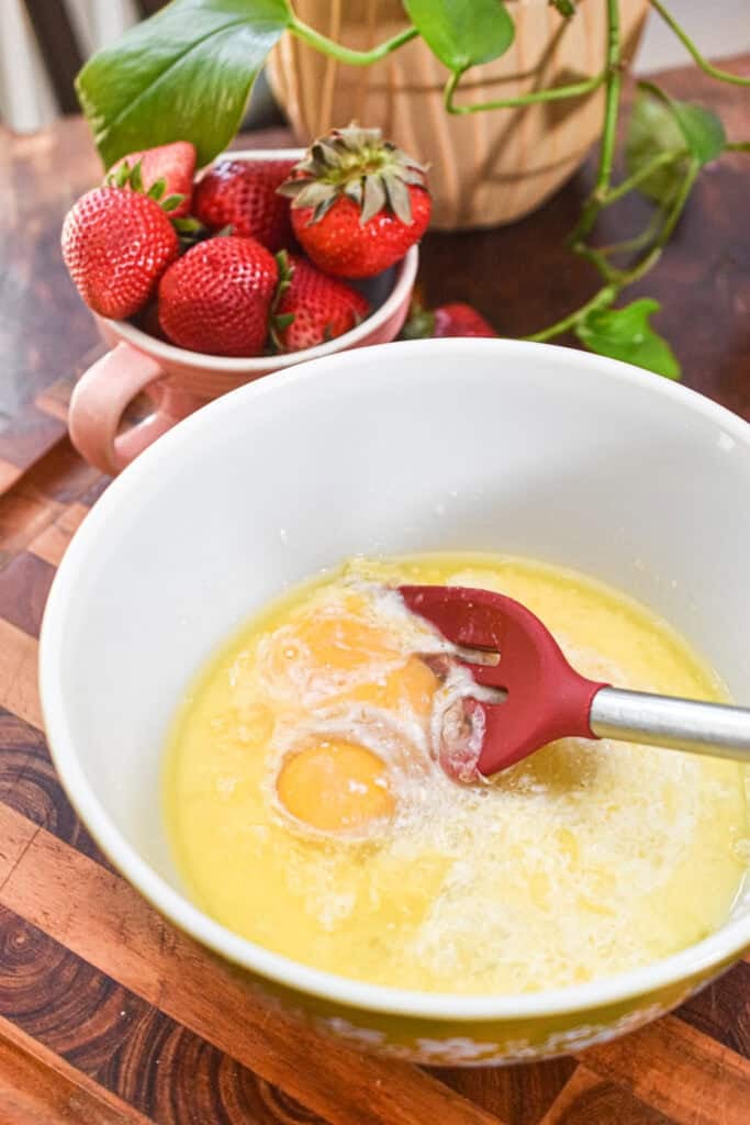 Mixing eggs and batter for bakery-style strawberry muffins in a white bowl.