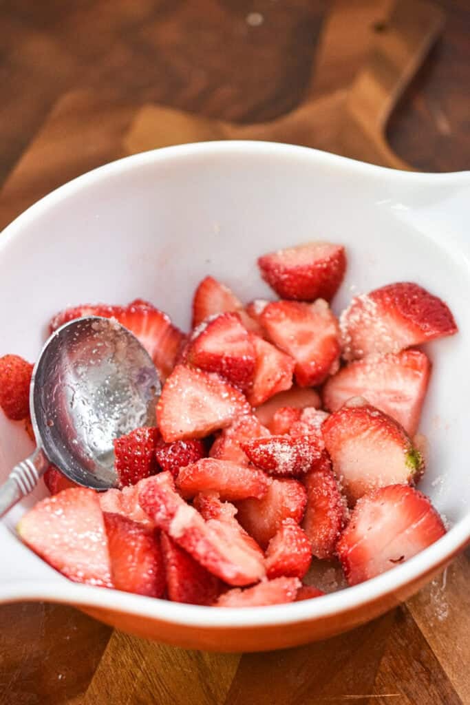 The sugar is mixed with the sliced strawberries.