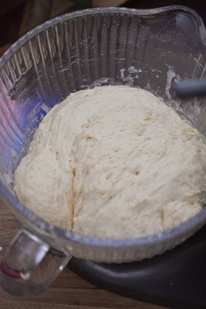 The dough has risen in the glass bowl of the stand mixer.