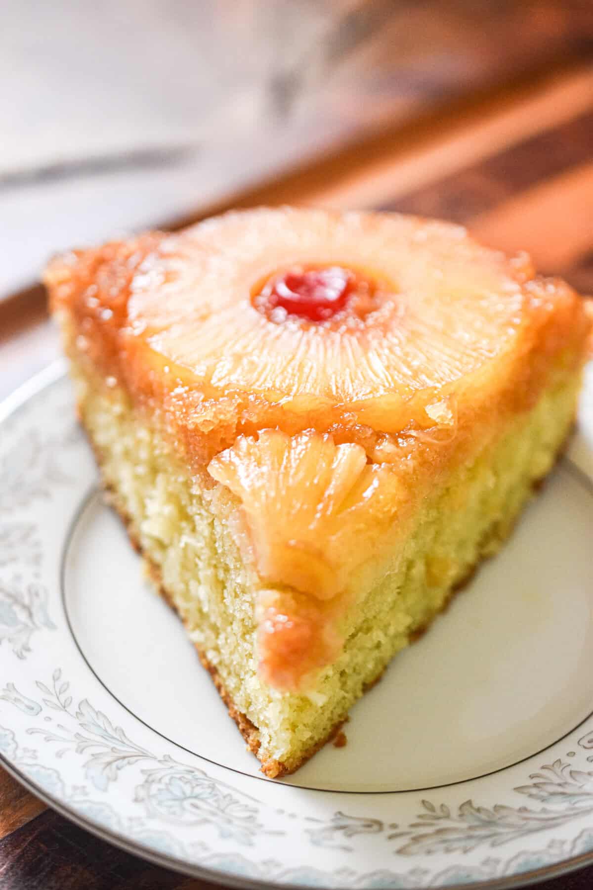 A slice of the sourdough pineapple upside down cake is on a plate on a wooden background.