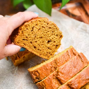 A hand is taking the 5 ingredient pumpkin bread slice out of the loaf.