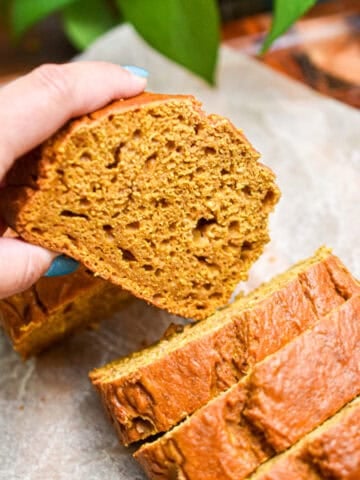 A hand is taking the 5 ingredient pumpkin bread slice out of the loaf.