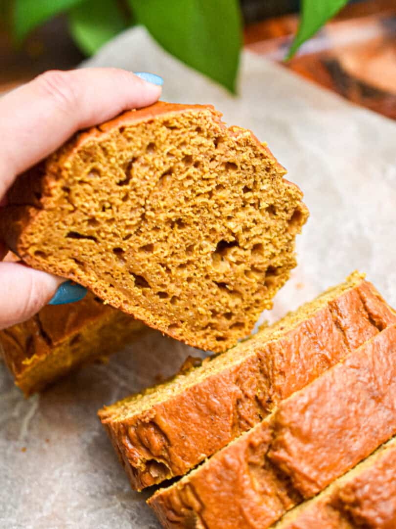 A hand is taking the 5 ingredient pumpkin bread slice out of the loaf.