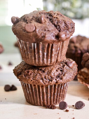 Two double chocolate sourdough muffins are stacked on top of each other with chocolate chips around them.