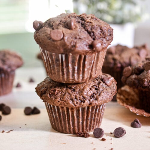 Two double chocolate sourdough muffins are stacked on top of each other with chocolate chips around them.