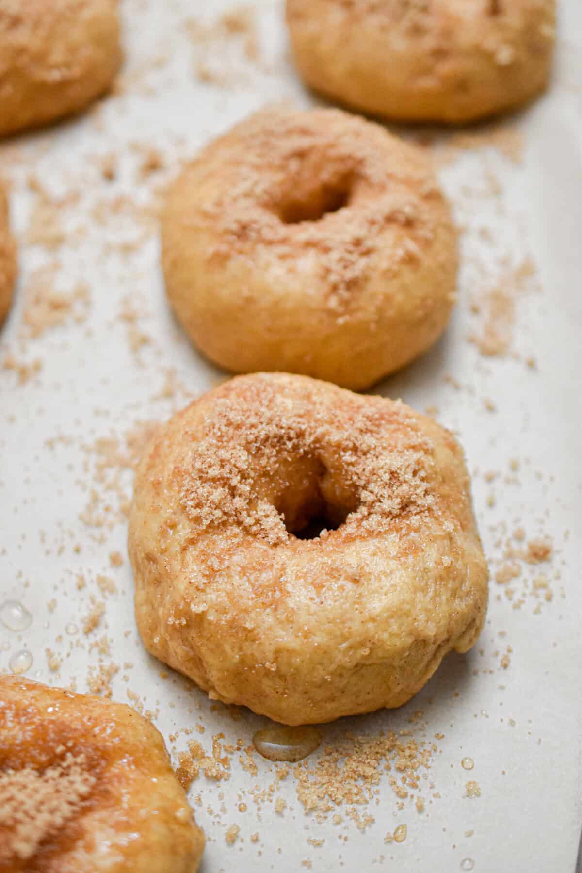 Cinnamon and sugar is added to the top of the bagels on parchment paper.