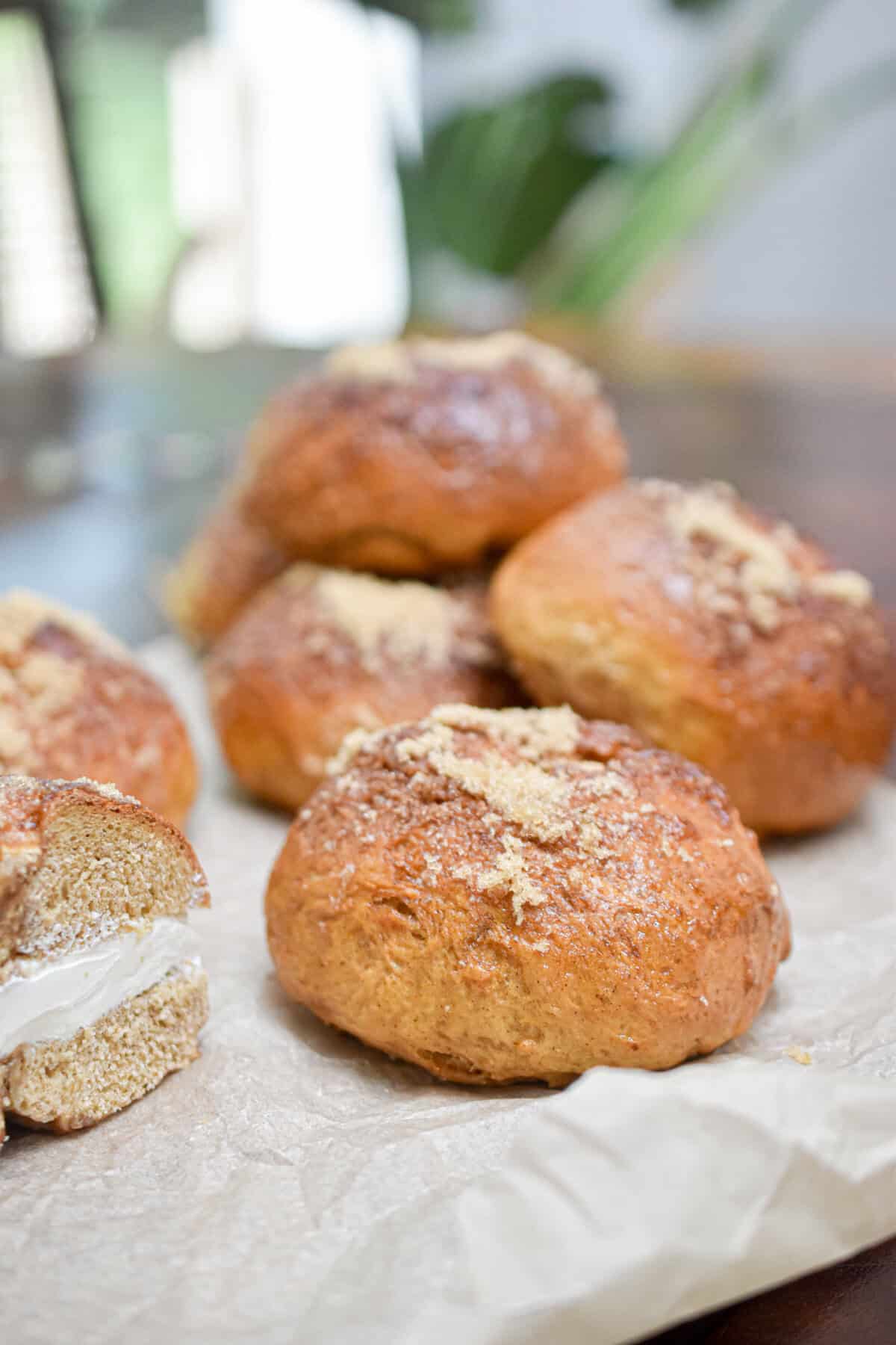 The sourdough discard pumpkin bagels with a cinnamon sugar crust are on a parchment paper with a half of a bagel with cream cheese is cut in half next to it.