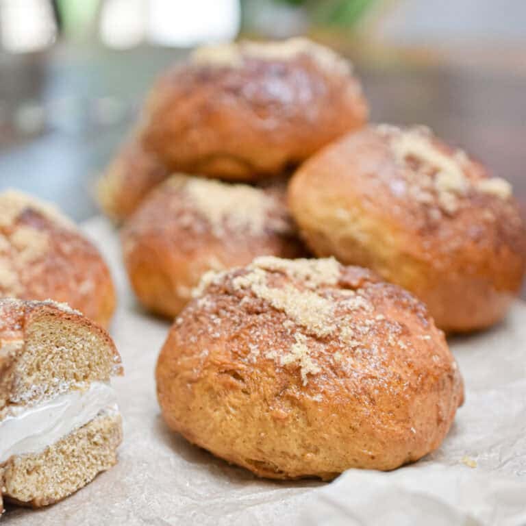 A sourdough discard pumpkin bagel is next to a half of a bagel with cream cheese on parchment paper.