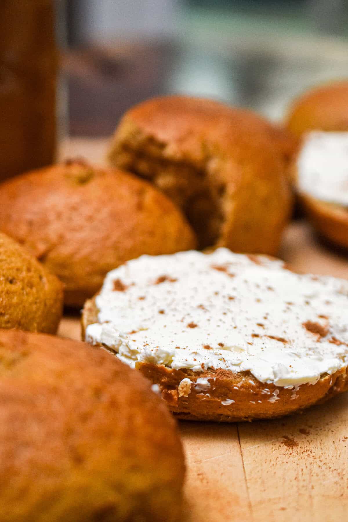 The sourdough pumpkin bagel is cut in half and cream cheese is all over the half of the bagel.