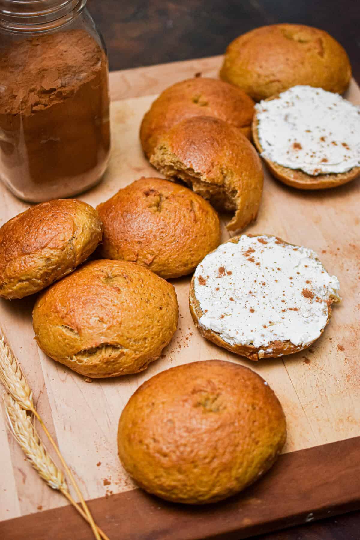 Two halves of sourdough pumpkin bagels are topped with cream cheese and surrounded by other bagels.