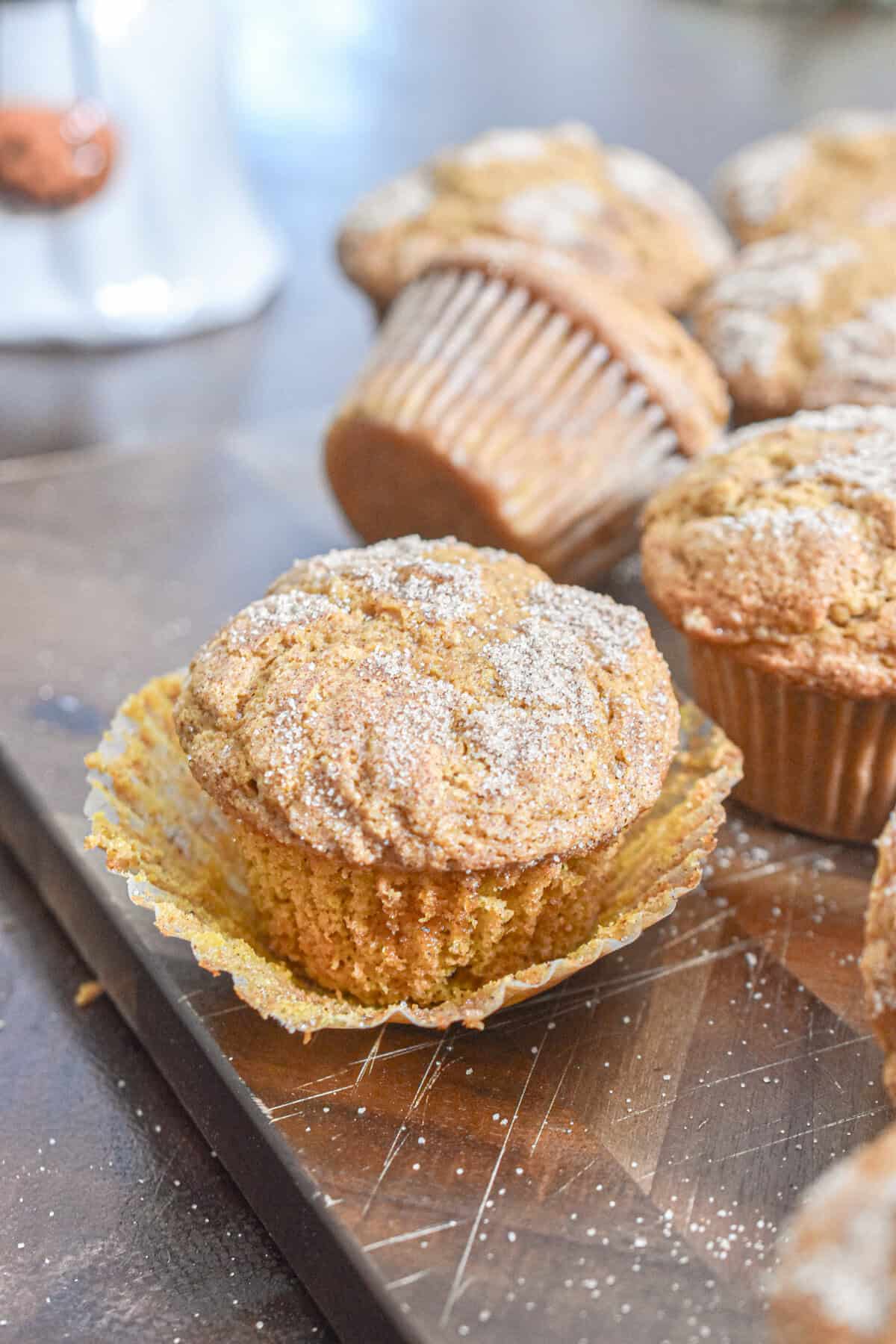 A muffin is opened on a cutting board with the rest of the muffins behind that one muffin.