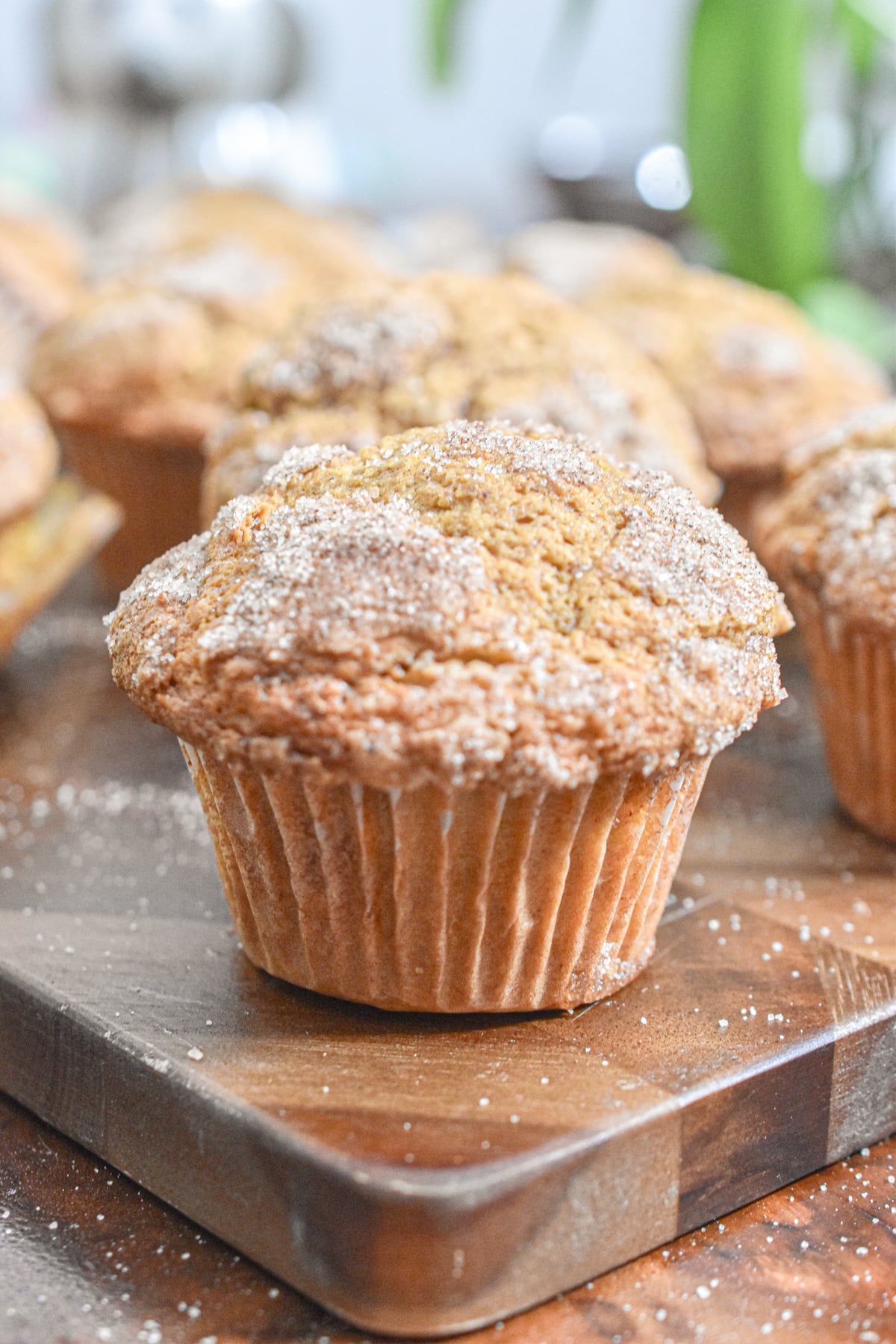 A pumpkin muffins with self rising flour is on a cutting board with the rest of the muffins in the background.