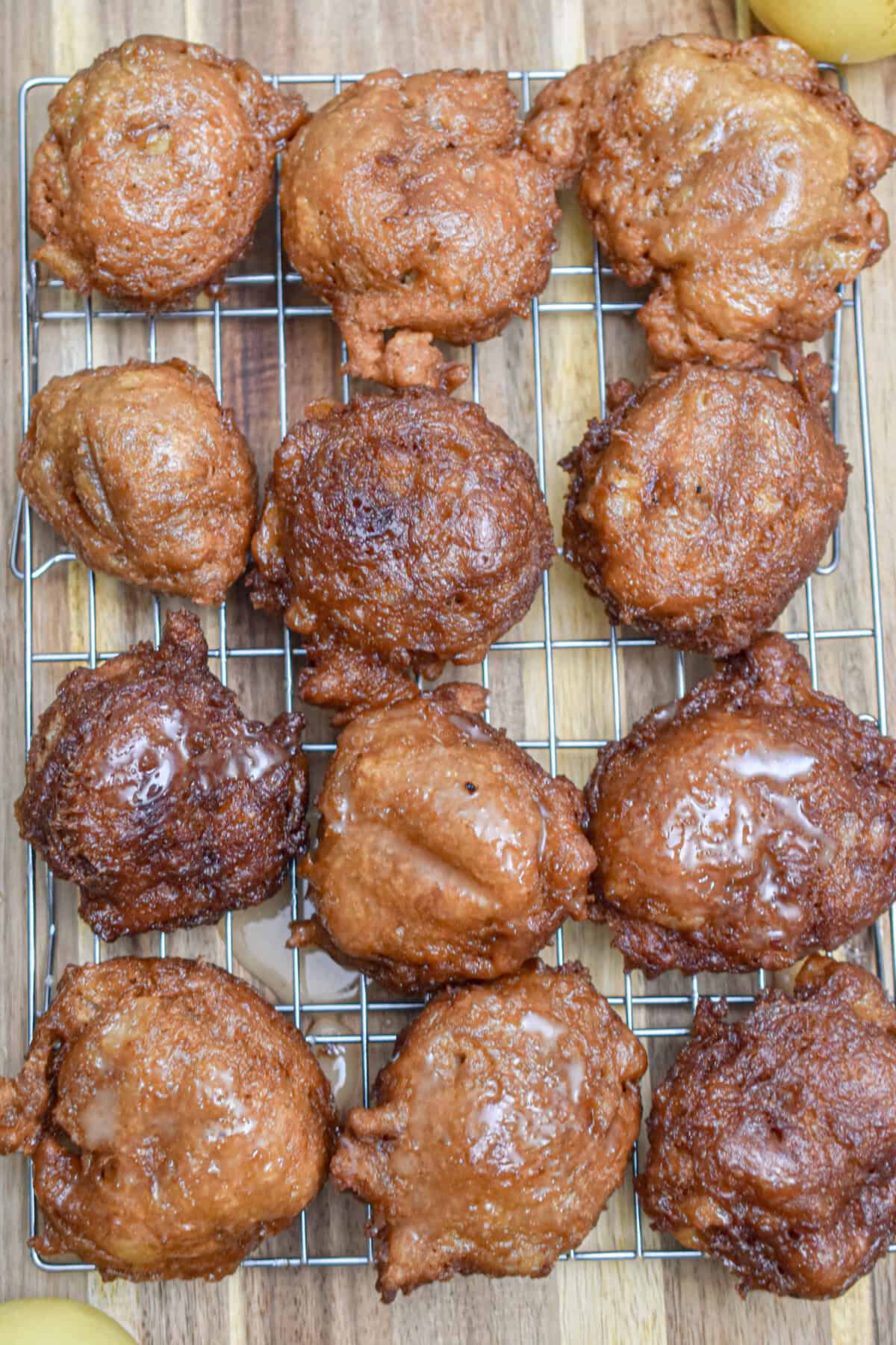 12 Sourdough discard apple fritters are on a wire rack on a wooden cutting board.