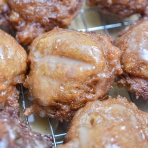 The sourdough discard apple fritters are covered with icing on a wire rack.