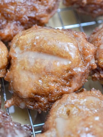 The sourdough discard apple fritters are covered with icing on a wire rack.