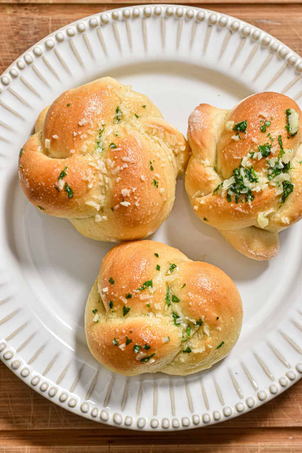 Three sourdough garlic knots with discard are on a plate on a wooden cutting board.
